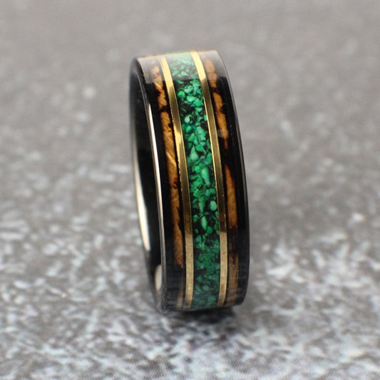 An 8mm wide black tungsten ring featuring a rich whiskey barrel wood inlay. A vibrant green malachite center line is bordered by two narrow bands of yellow gold, adding a bold yet refined touch.