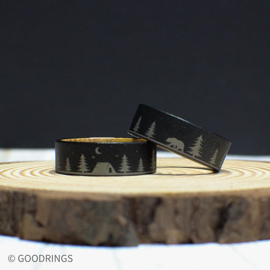 8mm tungsten wedding band with a detailed forest and camping scene engraved on the exterior, featuring trees, a tent, a bear, and stars. The interior is made of genuine whiskey barrel wood.