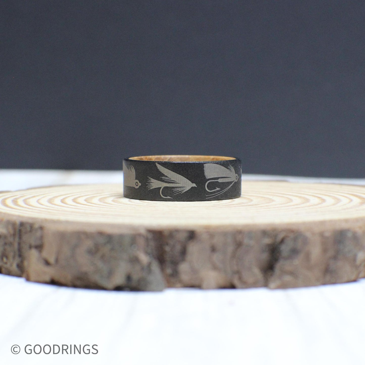 An 8mm tungsten ring with a whiskey barrel interior, engraved with fly fishing lures—perfect for any angler.