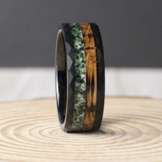 An 8mm black hammered tungsten ring featuring a dual inlay of charred whiskey barrel wood and crushed moss agate, blending rugged durability with natural beauty.