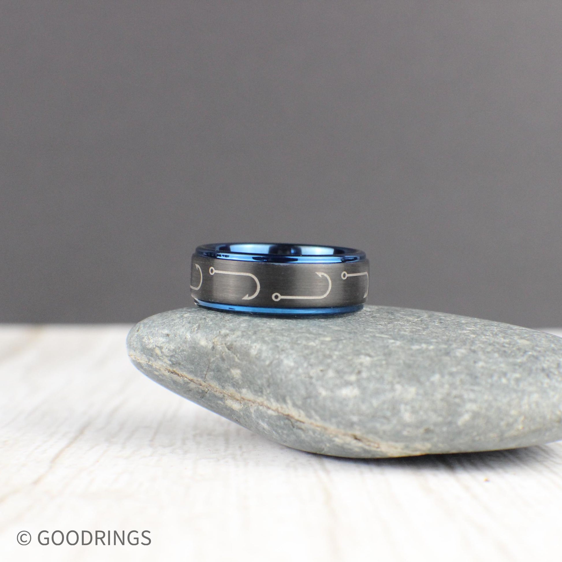An expertly crafted black tungsten ring with engraved fishing hooks that wrap around the 8mm band. The deep blue interior and edges add a striking contrast, making it a unique gift for fishermen and outdoor lovers. This comfort-fit ring is perfect for everyday wear or special occasions. Comes in a green and gold ring box inside a gift box, with a ring sizer and a free silicone ring included. Free resizing and returns for worry-free shopping.
