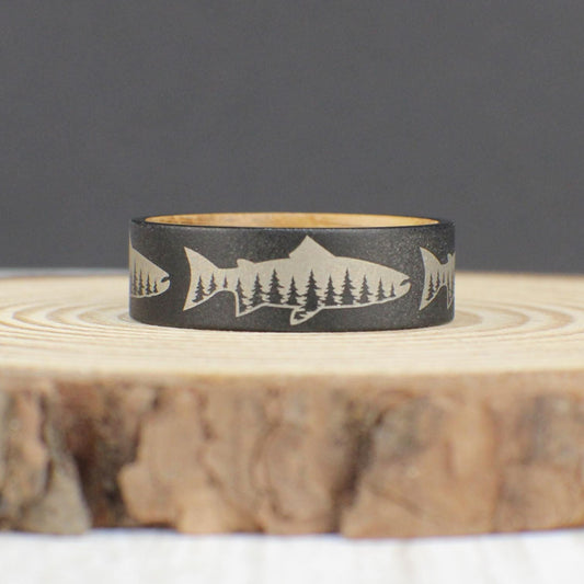Tungsten ring with sandblasted finish, engraved with a salmon silhouette featuring a tree line inside, and a whiskey barrel wood liner.
