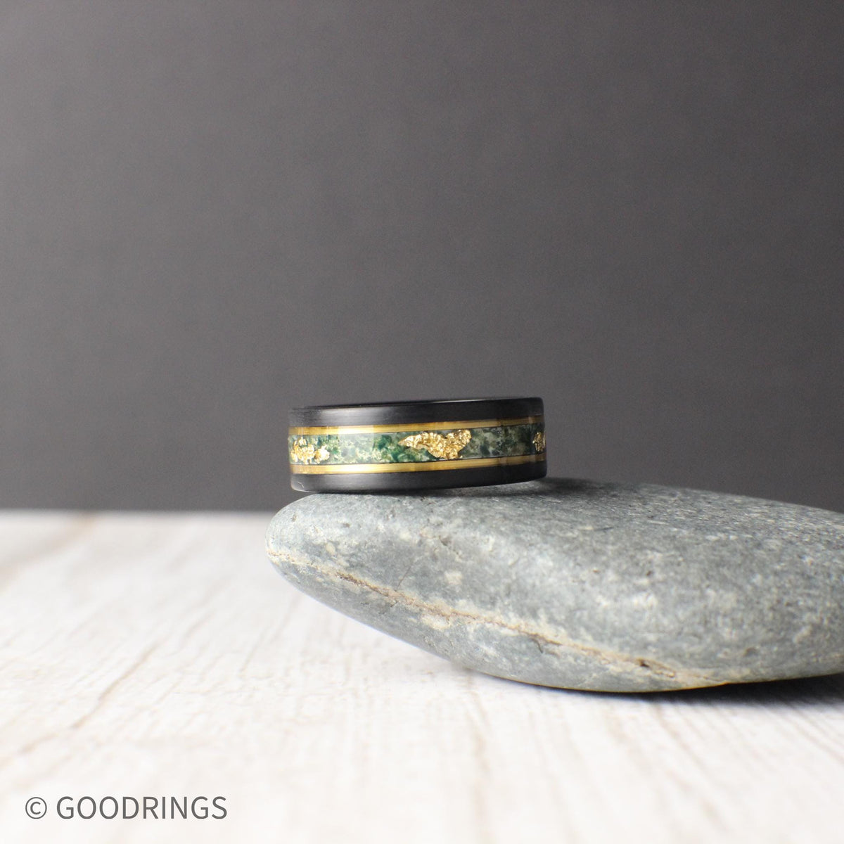 Durable black tungsten wedding band featuring a moss agate and gold leaf inlay, bordered by gold lines for a sleek look. Includes a gift box, silicone ring, and free ring sizer. Backed by a lifetime warranty, free exchanges, and hassle-free returns.