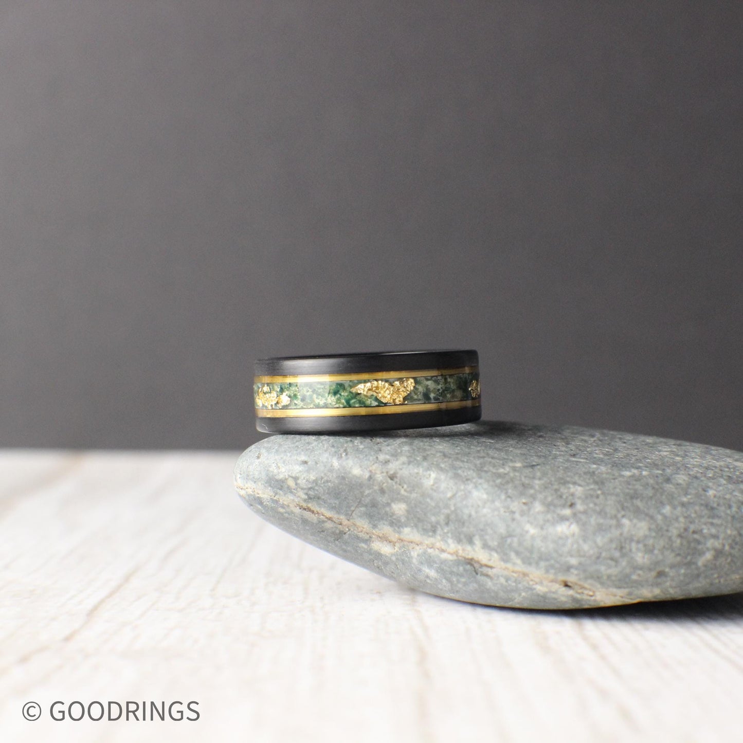 Durable black tungsten wedding band featuring a moss agate and gold leaf inlay, bordered by gold lines for a sleek look. Includes a gift box, silicone ring, and free ring sizer. Backed by a lifetime warranty, free exchanges, and hassle-free returns.