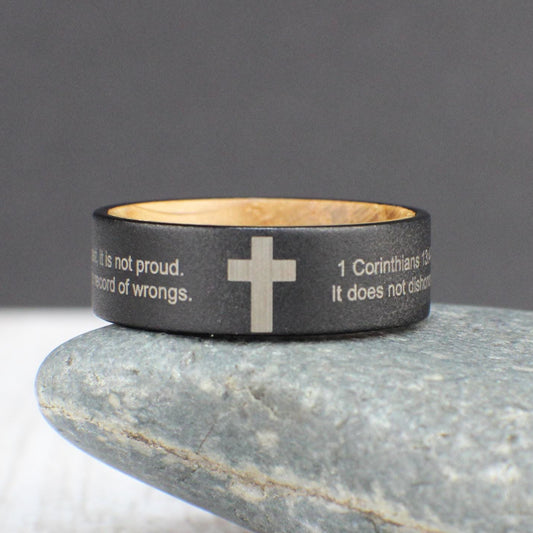 A custom cross ring featuring a sandblasted tungsten exterior with an engraved cross and a personalized Bible verse. The verse is wrapped around the cross in Arial font, with the size adjusted to fit. The inside is lined with sanded whiskey barrel wood for a smooth, comfortable fit, making it perfect for everyday wear.