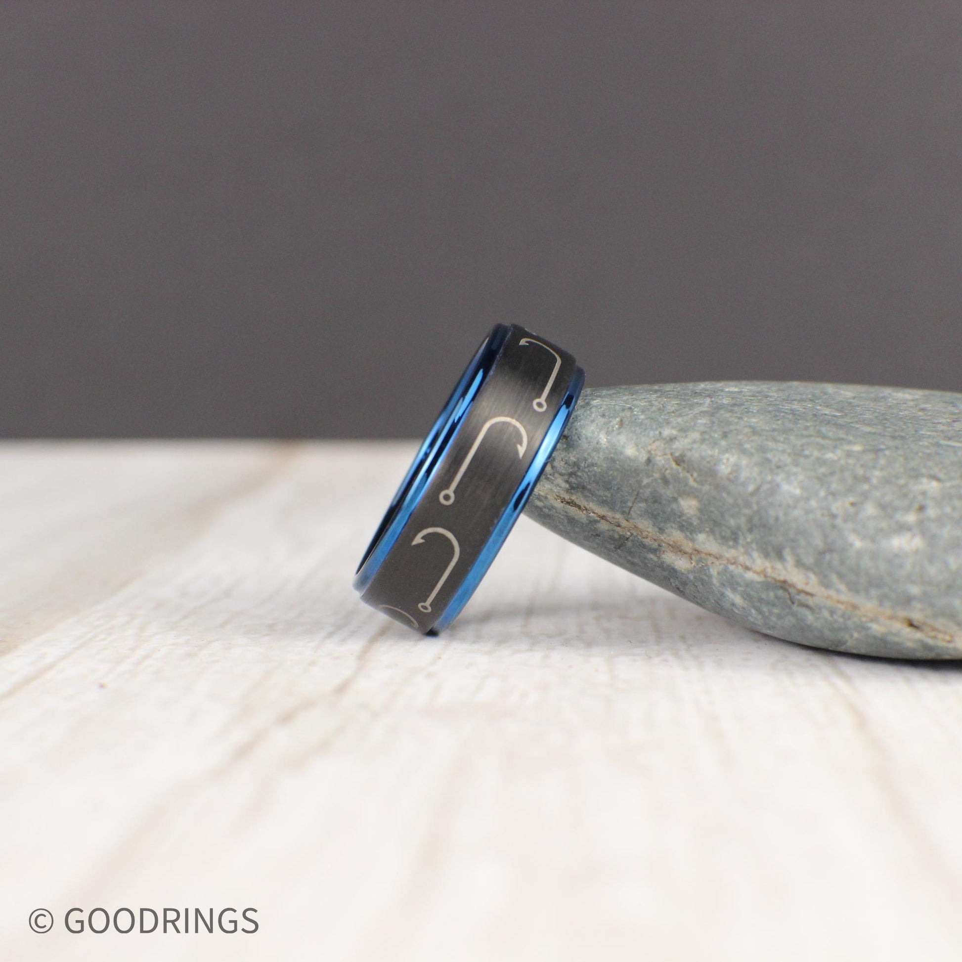 Designed for fishing enthusiasts, this engraved tungsten ring features a black brushed finish with fishing hooks circling the band. The dark blue edges and interior create a stunning contrast, making it a bold and stylish choice. This comfort-fit 8mm band is perfect as a wedding ring or gift. Comes in a green and gold ring box inside a gift box, with a ring sizer and free silicone ring included. Free resizing and returns available.