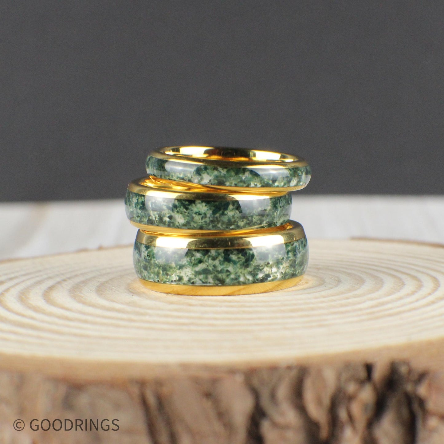 A timeless ring made of tungsten, known for its strength, plated in radiant yellow gold, and featuring a domed surface. The central inlay is crafted from genuine moss agate, showcasing unique, earthy green patterns. Sealed with a clear resin, the ring is both waterproof and scratch-resistant. Offered in 4mm, 6mm, and 8mm, this nature-inspired band makes a distinctive wedding ring or gift that combines rugged design with natural elegance.