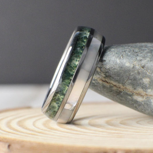 Domed tungsten wedding band with crushed moss agate and luminous moonstone inlays. The moss agate’s natural green and white marbling gives each ring an earthy, organic look, while the moonstone adds a sleek, glowing finish. Crafted with a comfort-fit interior and durable tungsten, this scratch-resistant ring is both timeless and unique, perfect as a men’s wedding ring, anniversary gift, or everyday band.