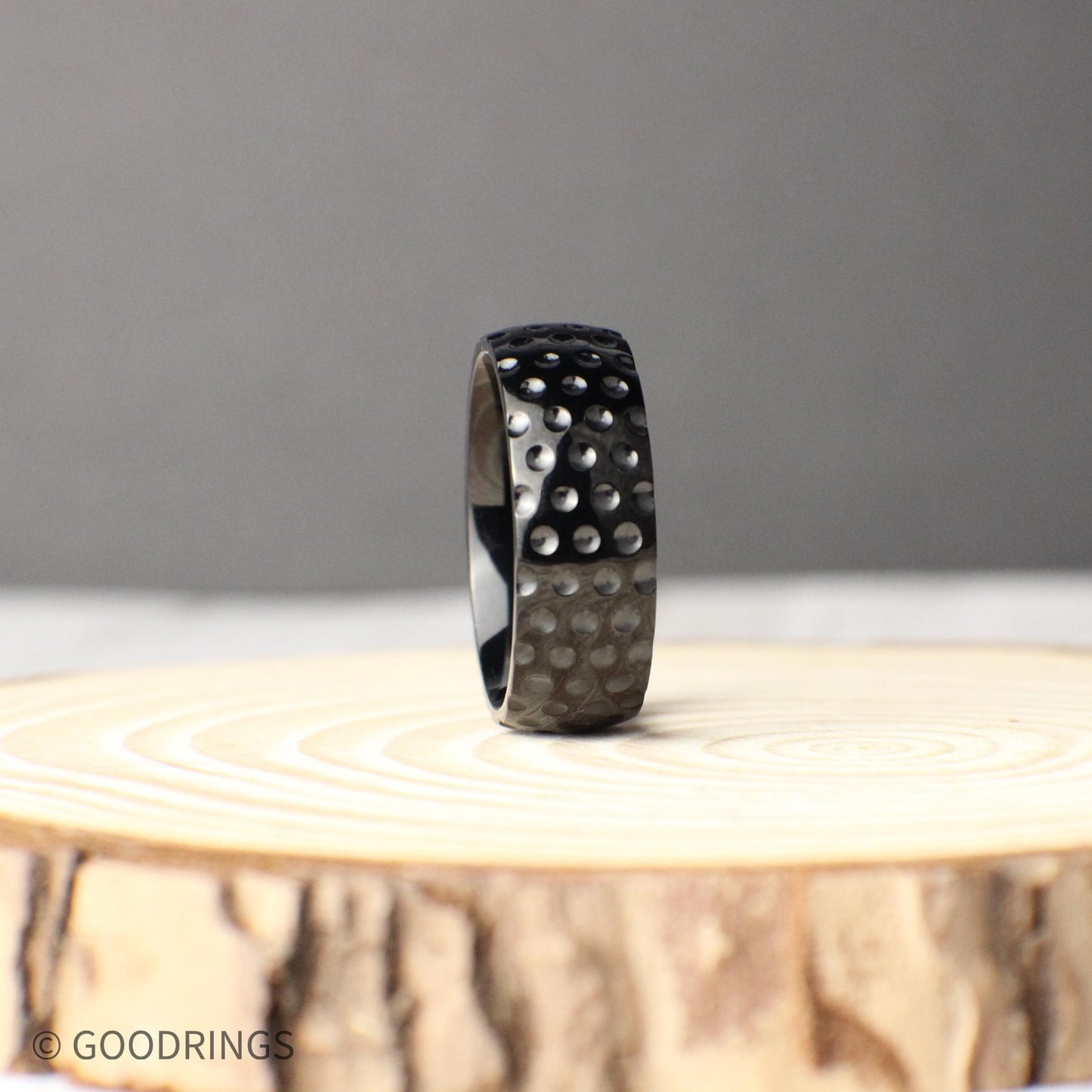 Black titanium ring with dimpled golf ball pattern, 8mm wide comfort fit band designed for long-lasting wear, photographed to show off its bold, masculine look, making it an ideal gift for golfers, anniversaries, or as a one-of-a-kind wedding ring that blends modern design with personal style.