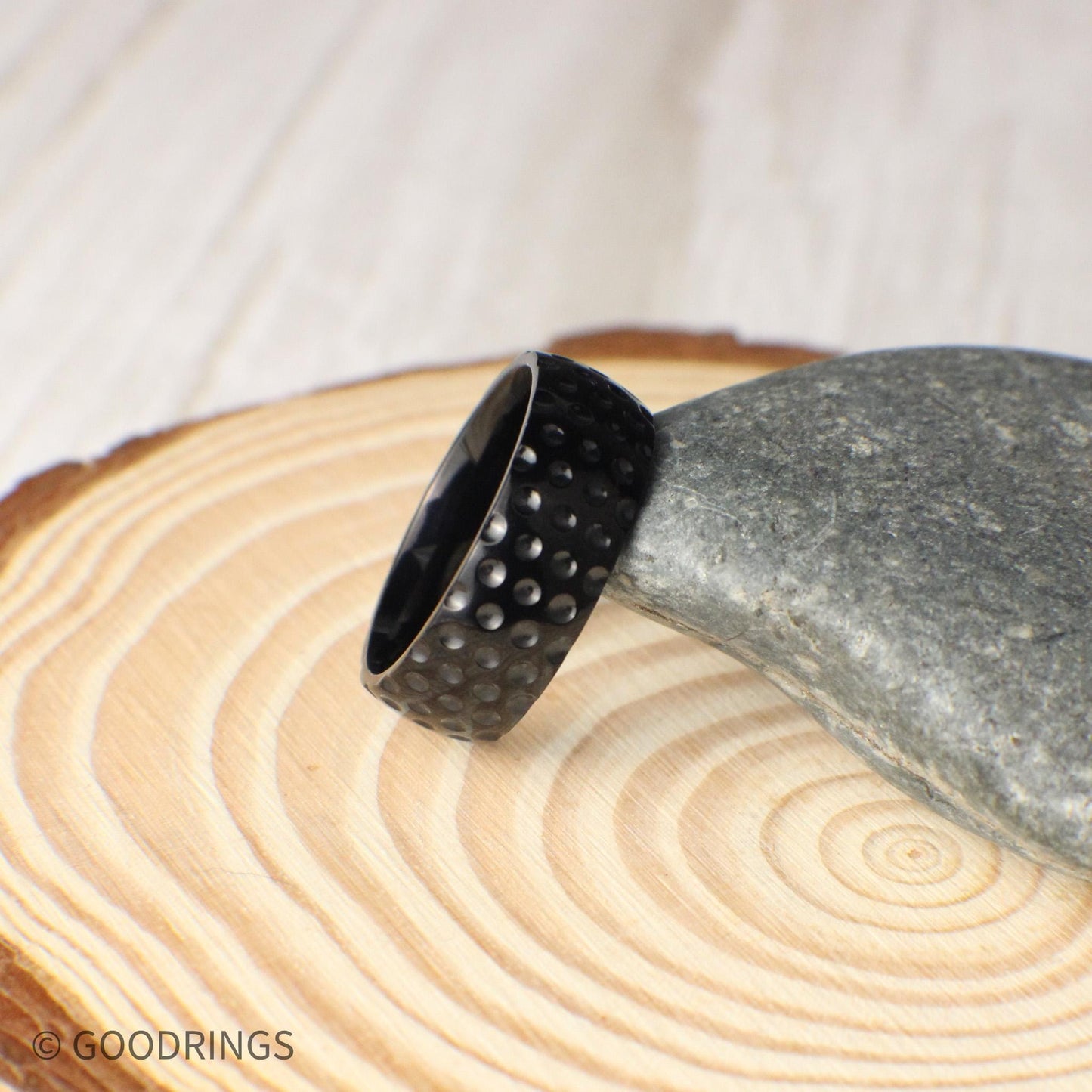 Modern titanium ring with golf ball texture in an 8mm width, shown resting on a smooth stone, highlighting the glossy black finish and patterned dimples that add depth and personality, making this a distinctive choice for men who appreciate golf and want a ring that reflects their passions.