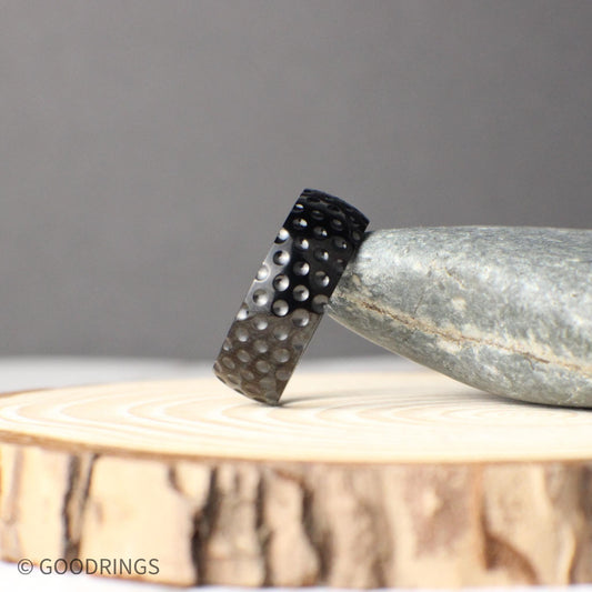Close-up photo of an 8mm titanium ring with a golf ball inspired texture, featuring a sleek black finish and round dimples across the band, symbolizing strength, durability, and sporty style, perfect for golf lovers seeking a unique wedding band or promise ring that stands out with its bold design.