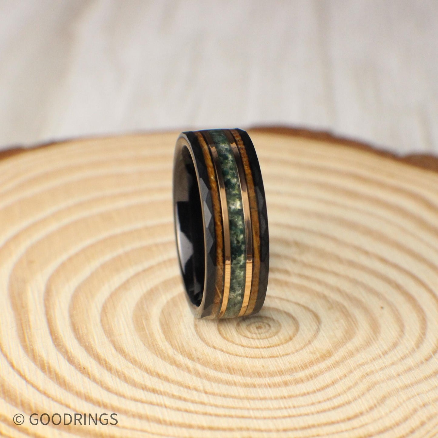 Elegant black tungsten ring, 8mm wide, designed with three distinct inlays: moss agate, 18K rose gold, and burnt whiskey barrel wood. The hammered finish enhances the rugged durability of tungsten, while the natural green agate, gleaming rose gold, and warm whiskey wood highlight artistry and meaning. A perfect band for weddings, anniversaries, or as a gift that tells a story of strength and love.