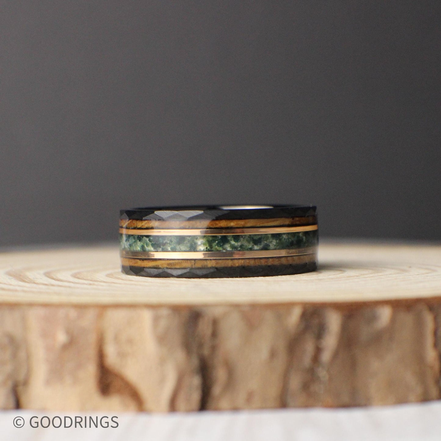 An 8mm wide men’s tungsten ring with a hammered black finish and a striking combination of moss agate, 18K rose gold, and whiskey barrel inlays. This band captures nature, craftsmanship, and sophistication in one design. The moss agate brings earthy greens, the rose gold adds sleek refinement, and the whiskey barrel wood represents rustic heritage. Ideal for weddings, anniversaries, or everyday wear.