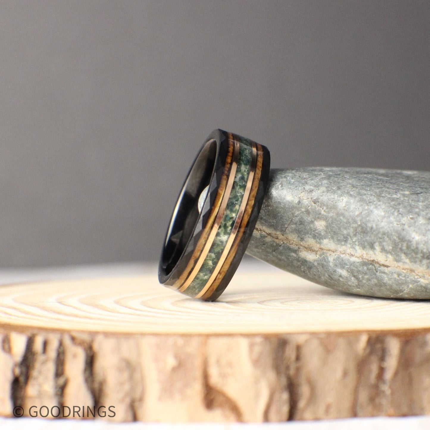 Black tungsten wedding band with 8mm width, showcasing inlays of moss agate, 18K rose gold, and whiskey barrel wood. The hammered black tungsten exterior is durable and modern, contrasted by the organic texture of moss agate, the glowing rose gold accent, and the rustic whiskey barrel finish. A unique, timeless ring design that symbolizes strength, history, and elegance for any special occasion.