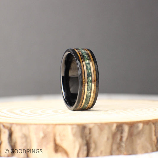 A bold 8mm black tungsten ring featuring a triple inlay of moss agate, 18K rose gold, and burnt whiskey barrel wood. The hammered tungsten band provides a rugged yet refined foundation, while the green moss agate adds natural vibrance, the rose gold line brings warmth, and the whiskey barrel wood offers a rustic character. Perfect as a wedding band, anniversary ring, or meaningful everyday piece.