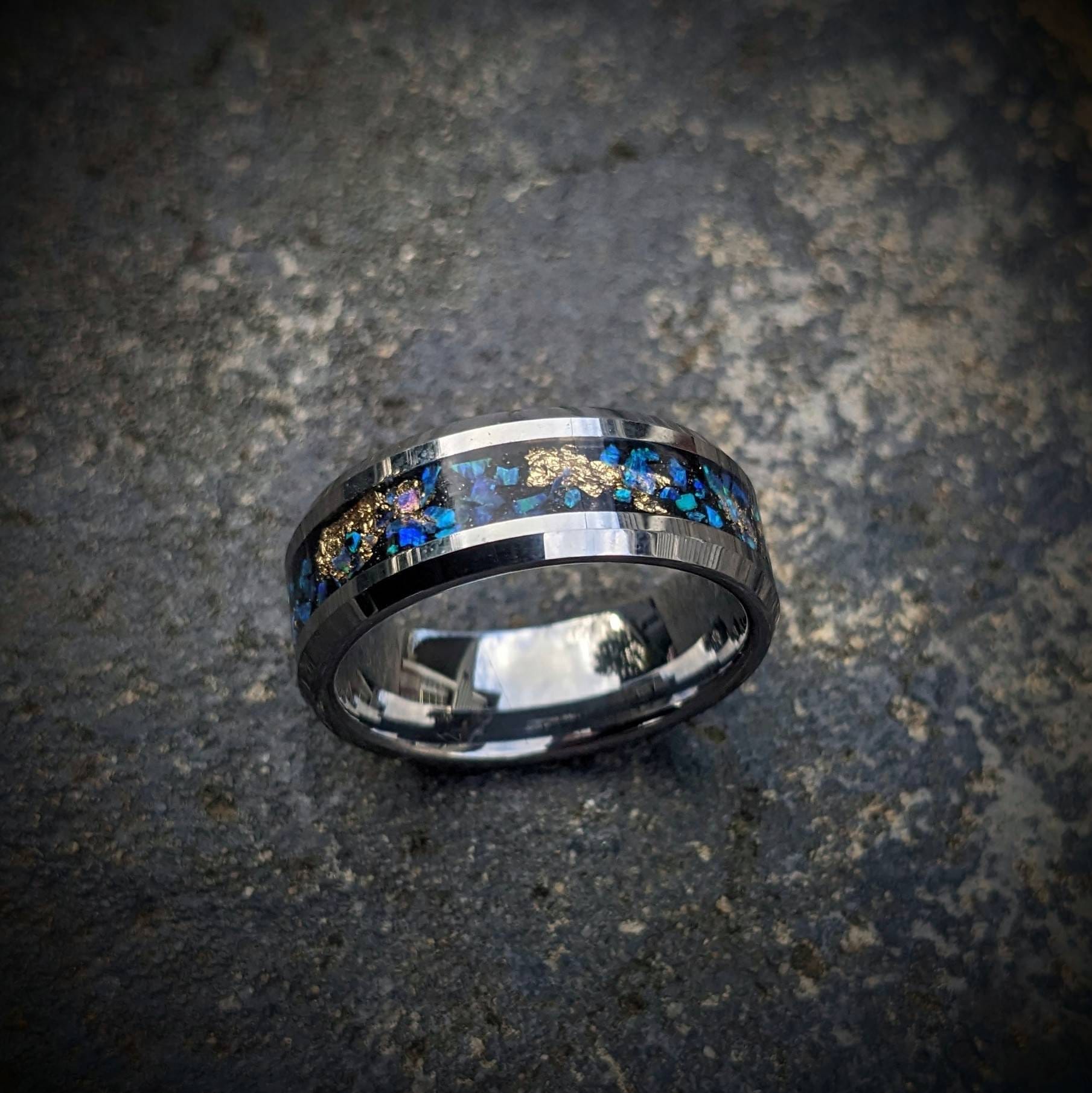 Our galaxy-inspired tungsten ring is crafted with dazzling blue opals and intricate gold leaf inlays that evoke the breathtaking beauty of the night sky. The polished tungsten band offers superior durability and a smooth, comfortable fit. This ring is perfect as a statement accessory or a meaningful gift, combining luxury with celestial charm. It’s designed to inspire awe and remind you of the infinite possibilities that the universe holds each time you wear it.