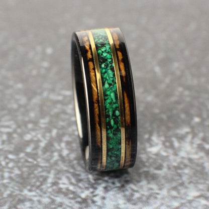 An 8mm wide black tungsten ring featuring a rich whiskey barrel wood inlay. A vibrant green malachite center line is bordered by two narrow bands of yellow gold, adding a bold yet refined touch.