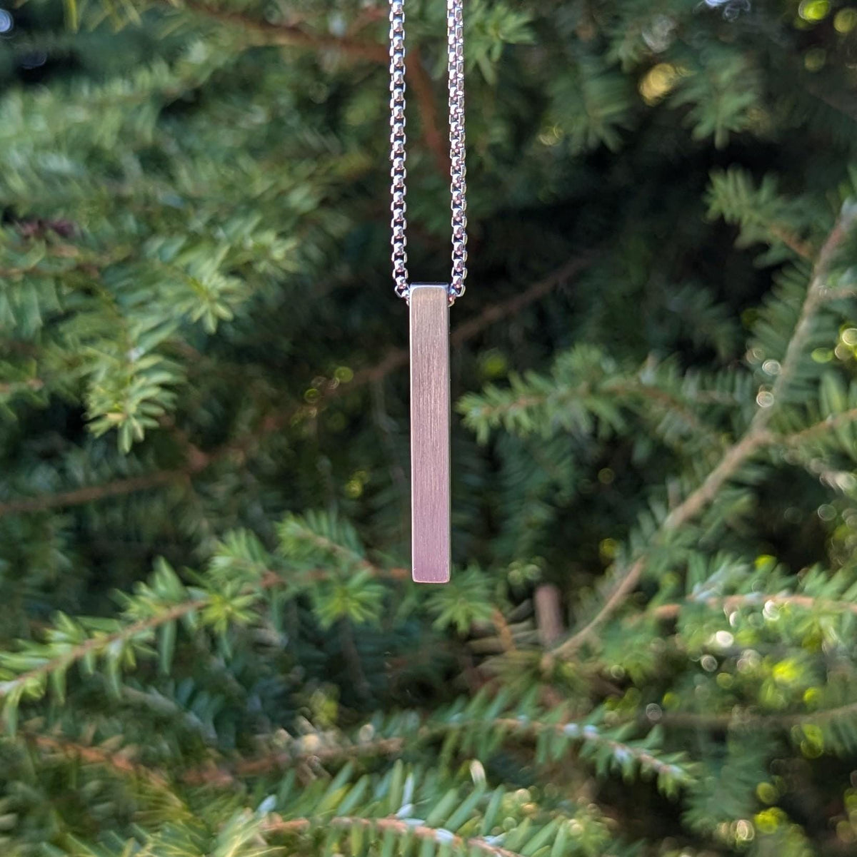 A minimalist stainless steel bar necklace with a scratch-resistant brushed finish, suspended on a sturdy 22-inch box chain, customizable on all four sides for a unique, personal design.