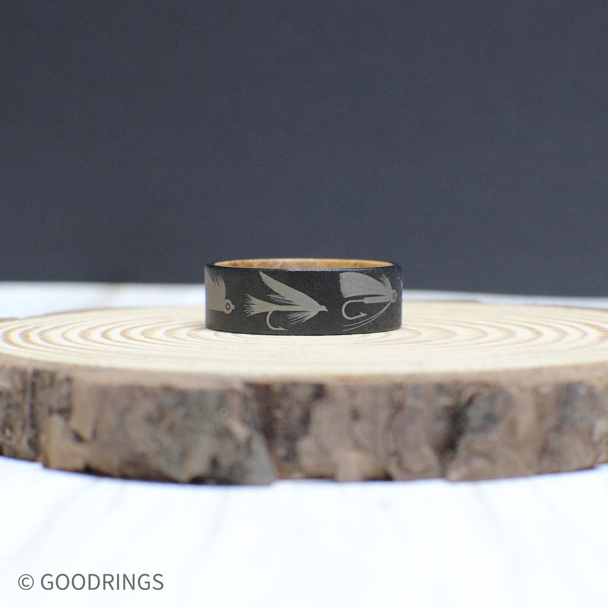 An 8mm tungsten ring with a whiskey barrel interior, engraved with fly fishing lures—perfect for any angler.