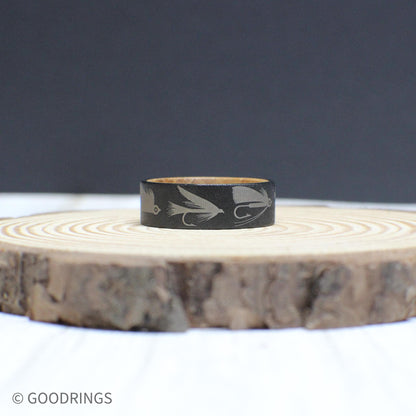 An 8mm tungsten ring with a whiskey barrel interior, engraved with fly fishing lures—perfect for any angler.