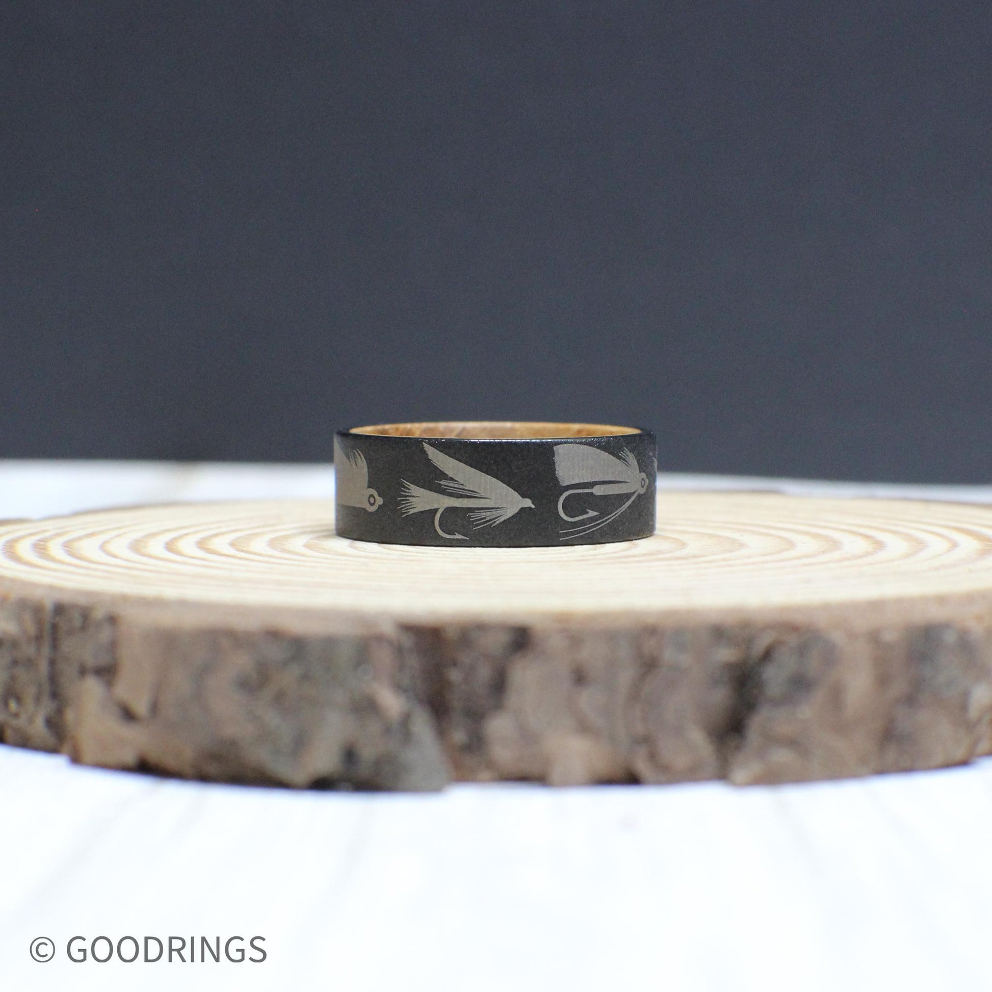 An 8mm tungsten ring with a whiskey barrel interior, engraved with fly fishing lures—perfect for any angler.