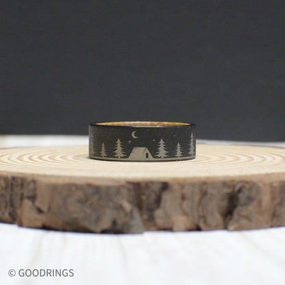 Tungsten ring showcasing an engraved outdoor scene with trees, a tent, and a bear under a starlit sky. The inside features warm whiskey barrel wood.