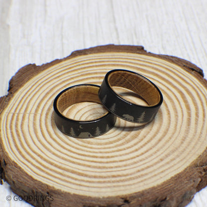 Close-up of the camping scene engraving on a tungsten wedding band, featuring trees, a tent, a bear, and stars, with whiskey barrel wood inside.