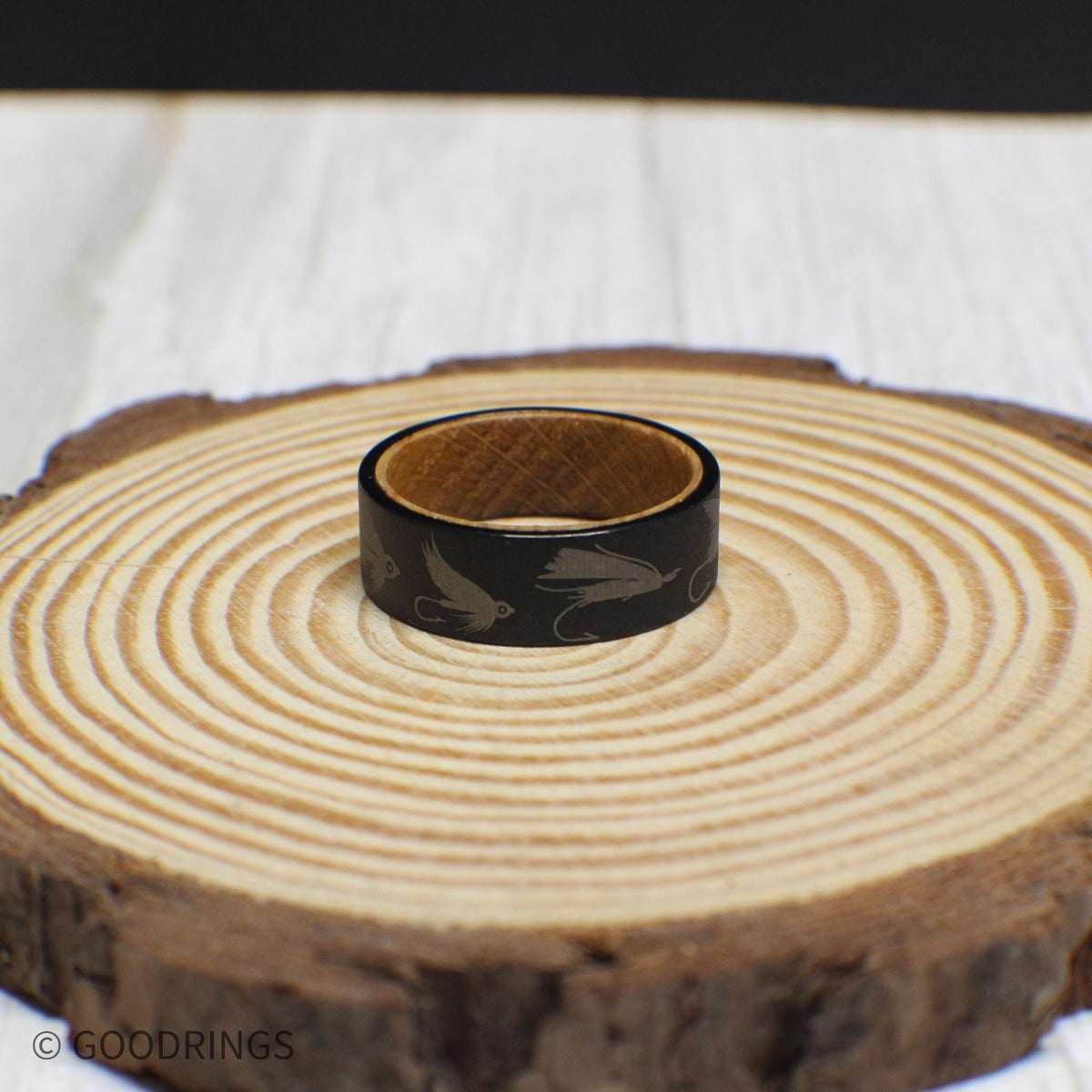 Tungsten fly fishing ring with a rugged sandblasted finish, engraved with lures, and lined with whiskey barrel wood.