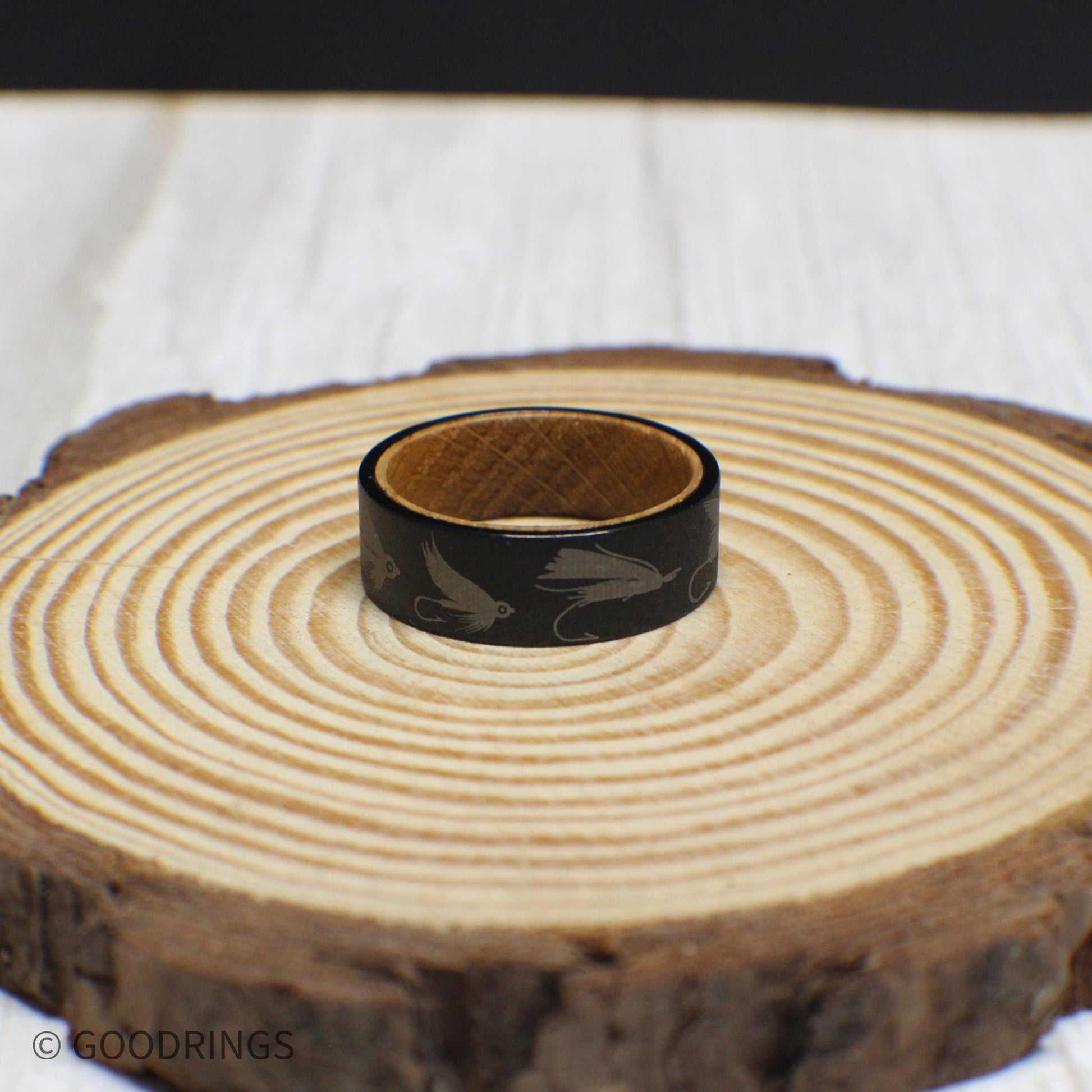 Tungsten fly fishing ring with a rugged sandblasted finish, engraved with lures, and lined with whiskey barrel wood.