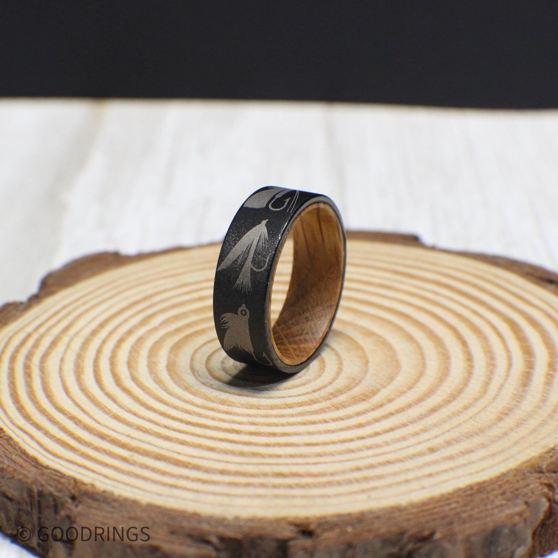 A durable tungsten ring featuring engraved fly fishing lures and a rustic whiskey barrel wood interior.