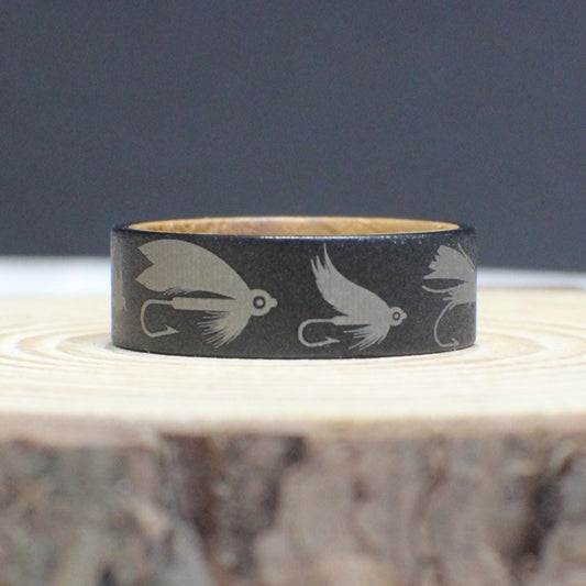 An 8mm tungsten fly fishing ring with a sandblasted finish, engraved with detailed fly fishing lures. The interior is crafted from genuine whiskey barrel wood.