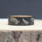An 8mm tungsten fly fishing ring with a sandblasted finish, engraved with detailed fly fishing lures. The interior is crafted from genuine whiskey barrel wood.