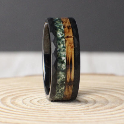 An 8mm black hammered tungsten ring featuring a dual inlay of charred whiskey barrel wood and crushed moss agate, blending rugged durability with natural beauty.