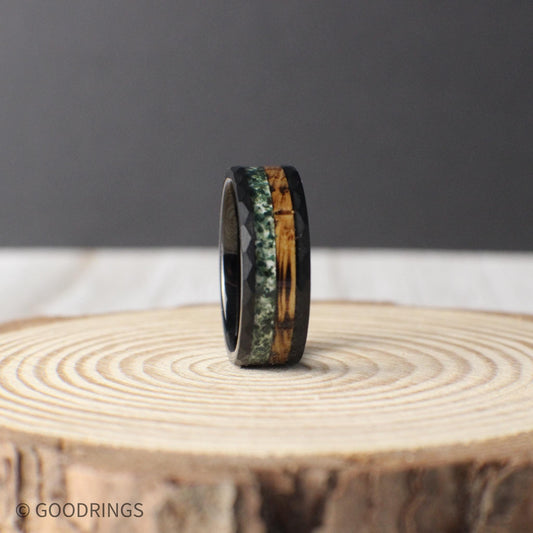 An 8mm black hammered tungsten ring featuring a dual inlay of charred whiskey barrel wood and crushed moss agate, blending rugged durability with natural beauty.