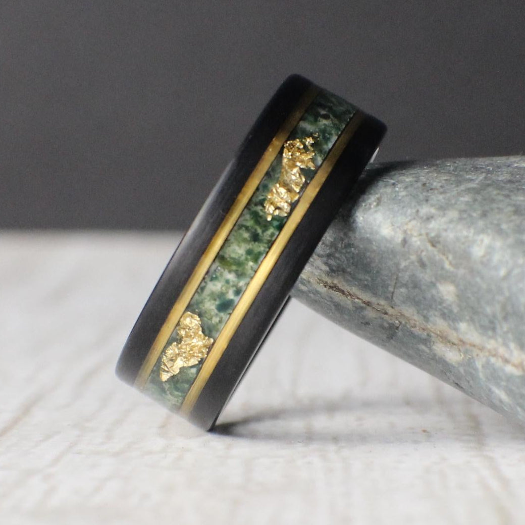 Black tungsten ring featuring a moss agate inlay with unique patterns and delicate gold leaf accents, bordered by gold lines for a refined finish. Includes a gift box, ring sizer, and silicone ring, with lifetime warranty and free exchanges.