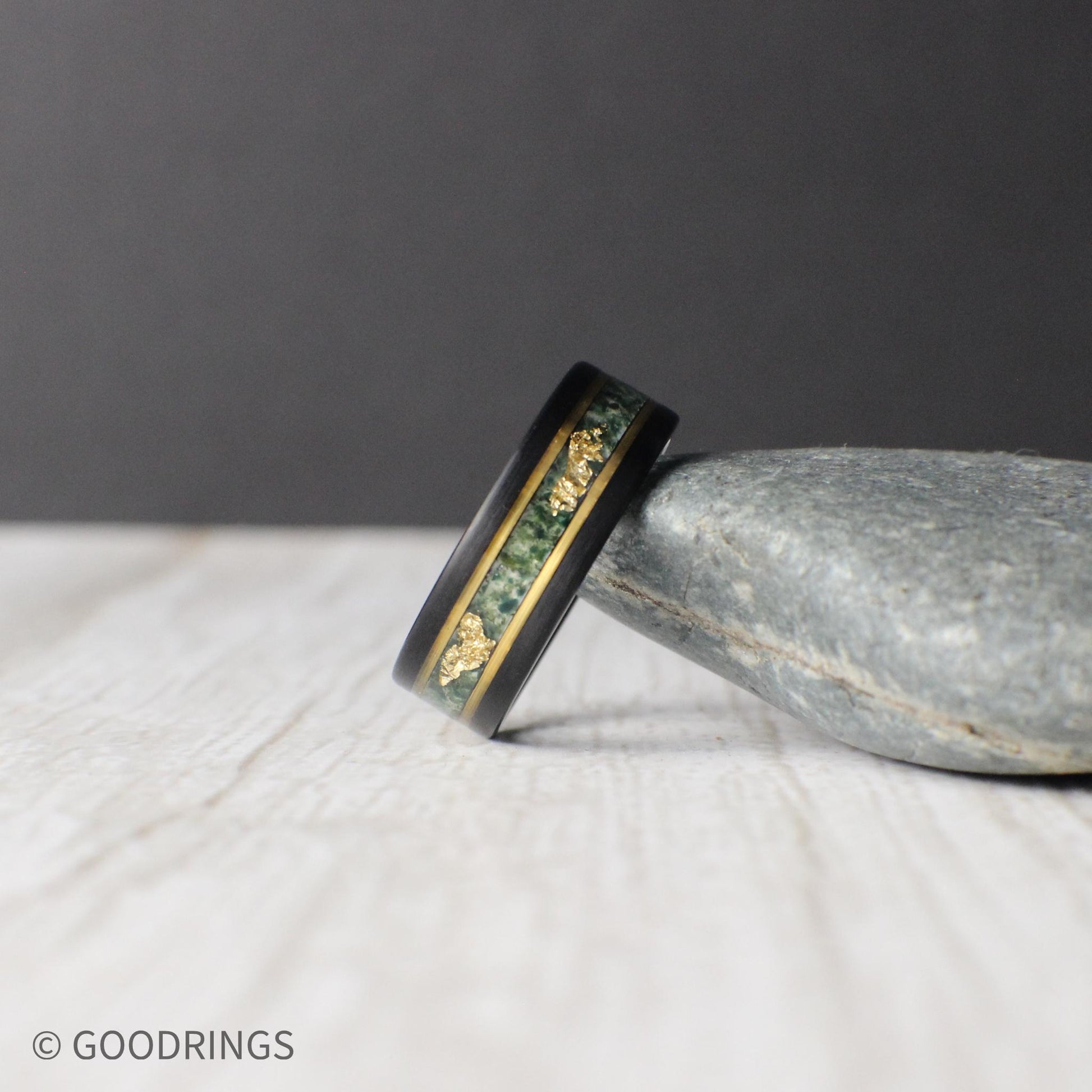Black tungsten ring featuring a moss agate inlay with unique patterns and delicate gold leaf accents, bordered by gold lines for a refined finish. Includes a gift box, ring sizer, and silicone ring, with lifetime warranty and free exchanges.