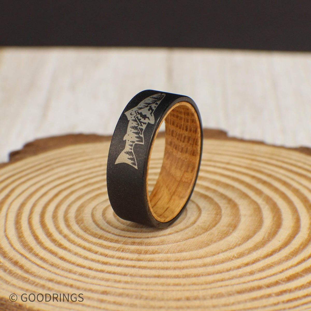This tungsten ring showcases a fish engraving on the outside, with a detailed mountain and tree design inside the fish. The interior is crafted from sanded whiskey barrel wood, offering a smooth and comfortable fit, ideal for nature lovers.