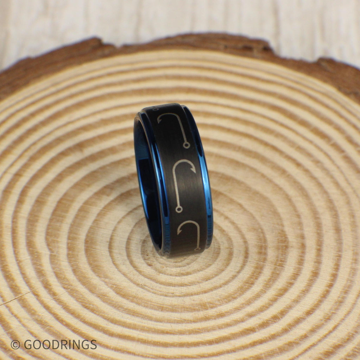 A durable tungsten fishing ring with a black brushed finish and engraved fishing hooks circling the band. The rich blue interior and edges add a striking pop of color, making it a standout piece. Ideal for fishermen, hunters, and outdoor enthusiasts. This 8mm comfort-fit band comes in a green and gold ring box inside a gift box, complete with a ring sizer and a silicone ring. Free resizing and returns for peace of mind.
