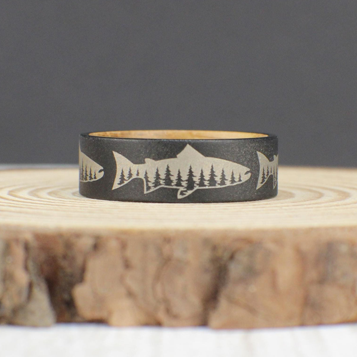 Tungsten ring with sandblasted finish, engraved with a salmon silhouette featuring a tree line inside, and a whiskey barrel wood liner.