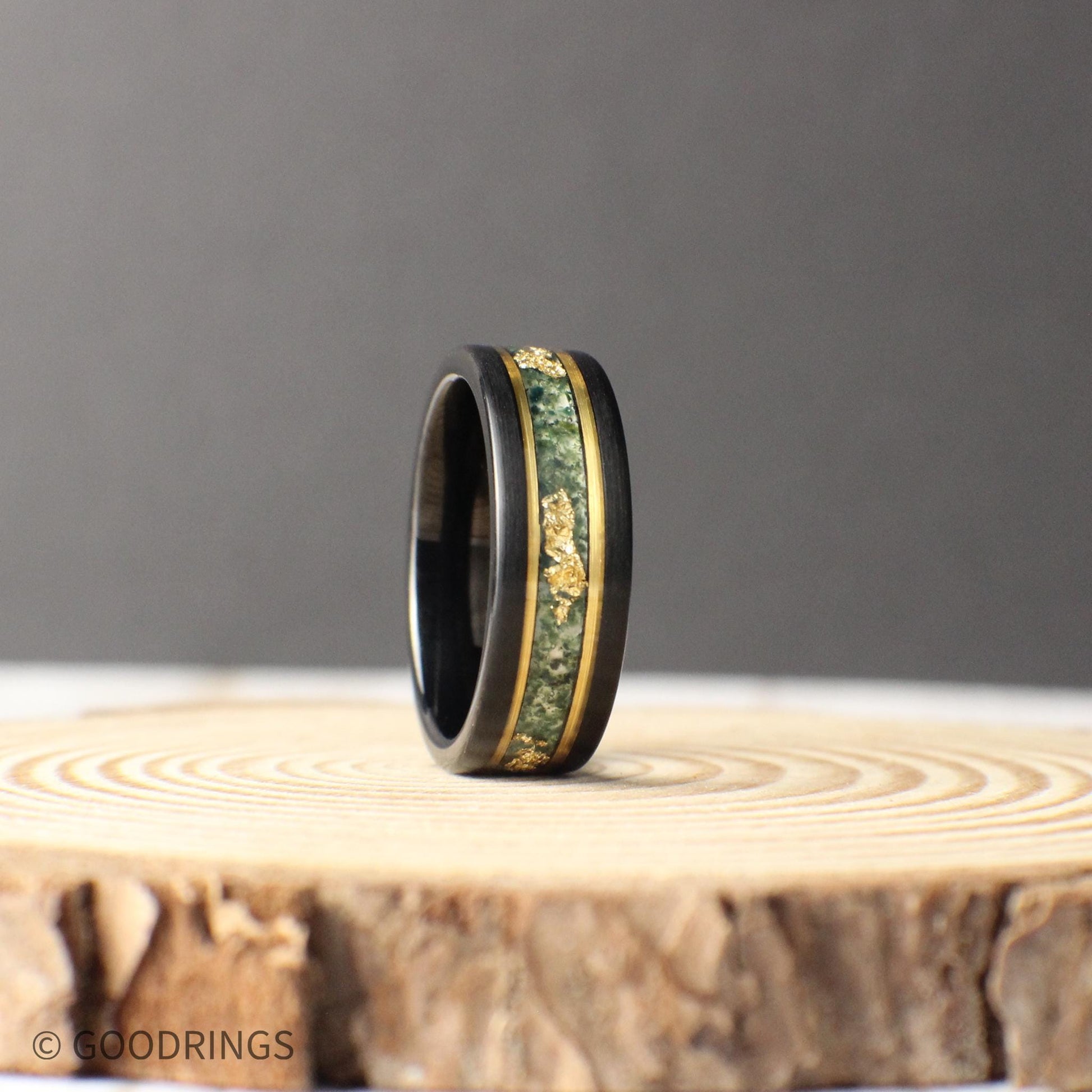 Elegant black tungsten wedding band with a moss agate inlay showcasing natural patterns and gold leaf details. Gold lines frame the inlay, adding sophistication. Comes with a ring box, free ring sizer, and silicone ring, plus lifetime warranty and hassle-free returns.