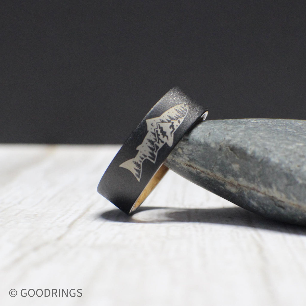 This tungsten ring features an engraved fish with a mountain and tree design on the exterior and smooth whiskey barrel wood lining inside. The comfort fit ensures it can be worn daily, making it a great gift for outdoor enthusiasts.