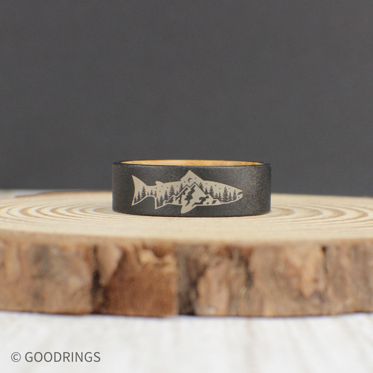 A durable tungsten ring with a sandblasted finish, featuring an engraved fish with a mountain and tree design inside. The inside of the ring is lined with sanded whiskey barrel wood for a comfortable fit. This ring makes a great gift for birthdays or Father’s Day.
