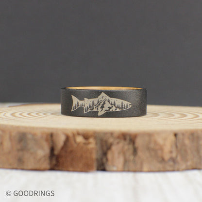 A durable tungsten ring with a sandblasted finish, featuring an engraved fish with a mountain and tree design inside. The inside of the ring is lined with sanded whiskey barrel wood for a comfortable fit. This ring makes a great gift for birthdays or Father’s Day.