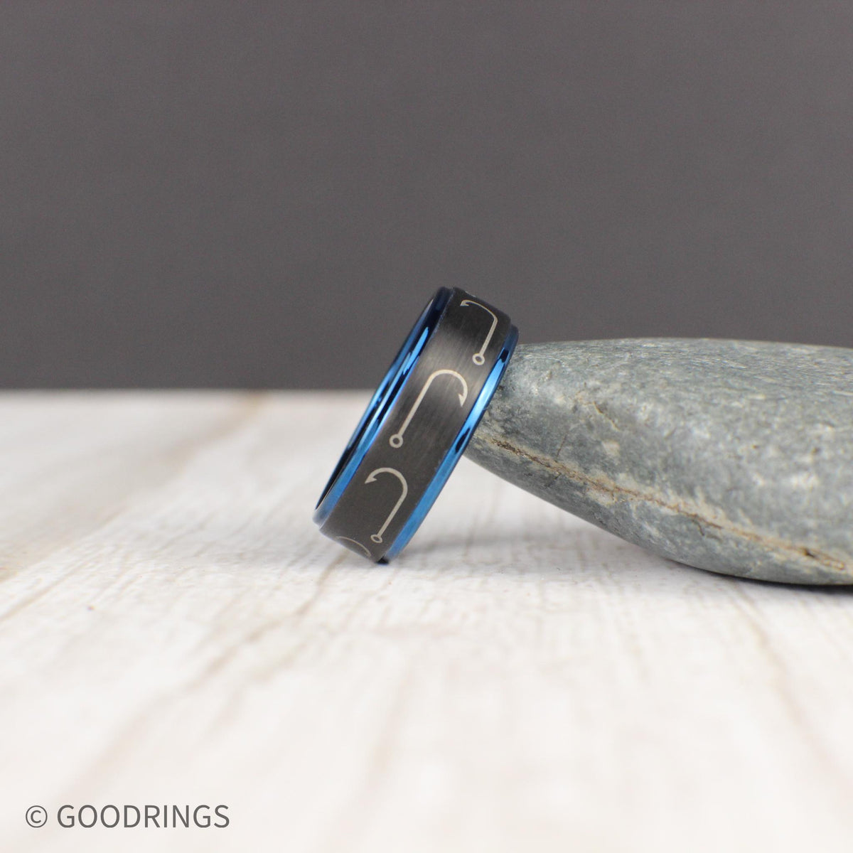 Designed for fishing enthusiasts, this engraved tungsten ring features a black brushed finish with fishing hooks circling the band. The dark blue edges and interior create a stunning contrast, making it a bold and stylish choice. This comfort-fit 8mm band is perfect as a wedding ring or gift. Comes in a green and gold ring box inside a gift box, with a ring sizer and free silicone ring included. Free resizing and returns available.