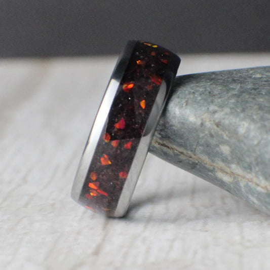 A handcrafted 8mm tungsten domed ring featuring a crushed red garnet inlay with red opal accents, creating a fiery, ember-like effect. The polished tungsten base provides a sleek, modern look, while the vibrant inlay offers depth and shimmer. Ideal as a unique men’s wedding band or statement piece for anyone who appreciates bold, nature-inspired design and lasting durability.