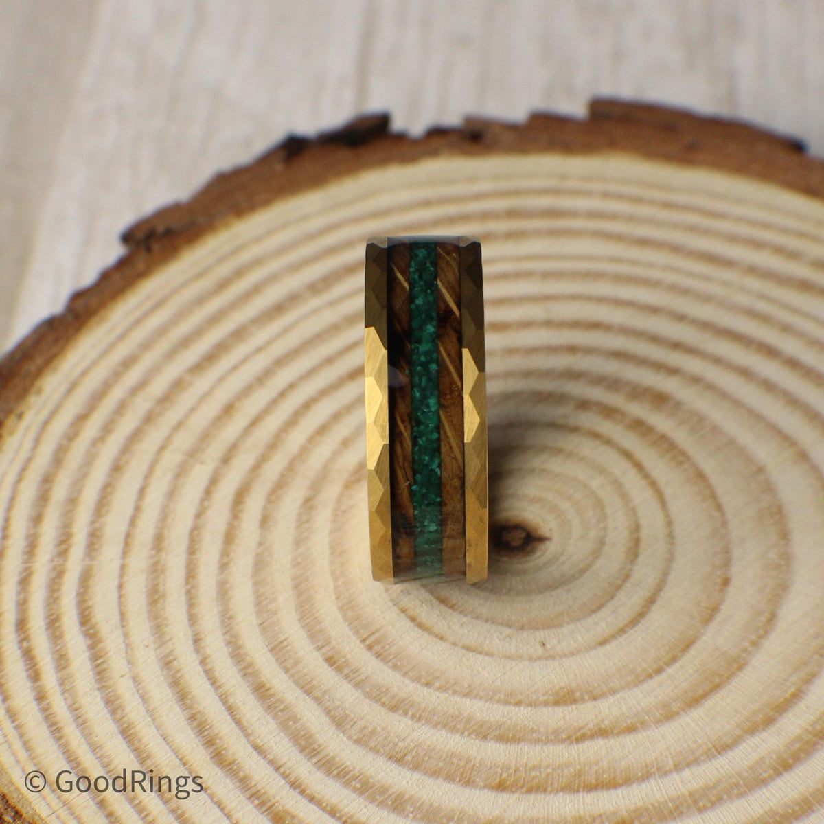 A nature-inspired tungsten ring with a gold hammered finish, offering strength and unique style. It features a dual inlay of burnt whiskey barrel wood and crushed moss agate, providing a mix of deep wood grain and rich green tones. Perfect for weddings, anniversaries, or everyday wear, this 6mm or 8mm ring stands out with its bold texture and natural details. A great choice for anyone who loves rustic, earthy designs.