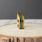 This hammered tungsten ring is plated in gold and features a natural inlay with two distinct materials. One section showcases charred whiskey barrel wood, adding warmth and texture, while a center line of crushed moss agate brings an organic green tone. The hammered texture enhances the rugged, handcrafted look. Available in 6mm or 8mm widths, this ring is great for daily wear or as a nature-inspired wedding band.