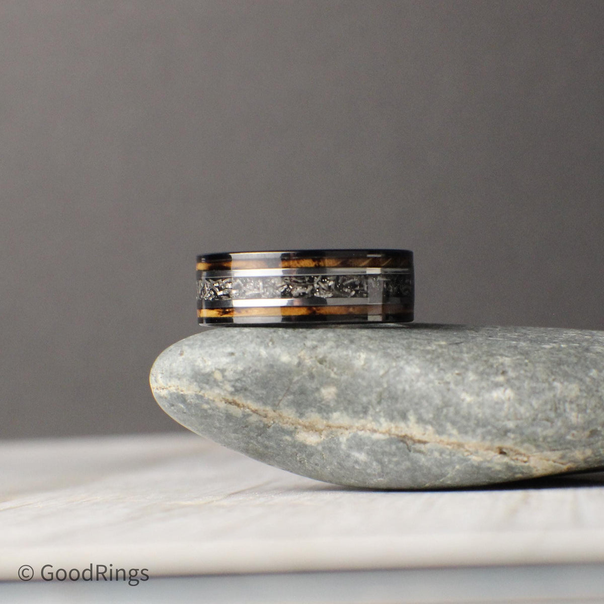 An 8mm tungsten wedding band that captures rustic charm and stellar significance. The ring features a warm inlay of burnt whiskey barrel wood, with a genuine meteorite stripe running through the center. Silver lines separate the materials, highlighting the textures and contrast. Perfect for engagements, weddings, or anniversaries, this ring is built to last and symbolizes a love that’s grounded yet limitless.