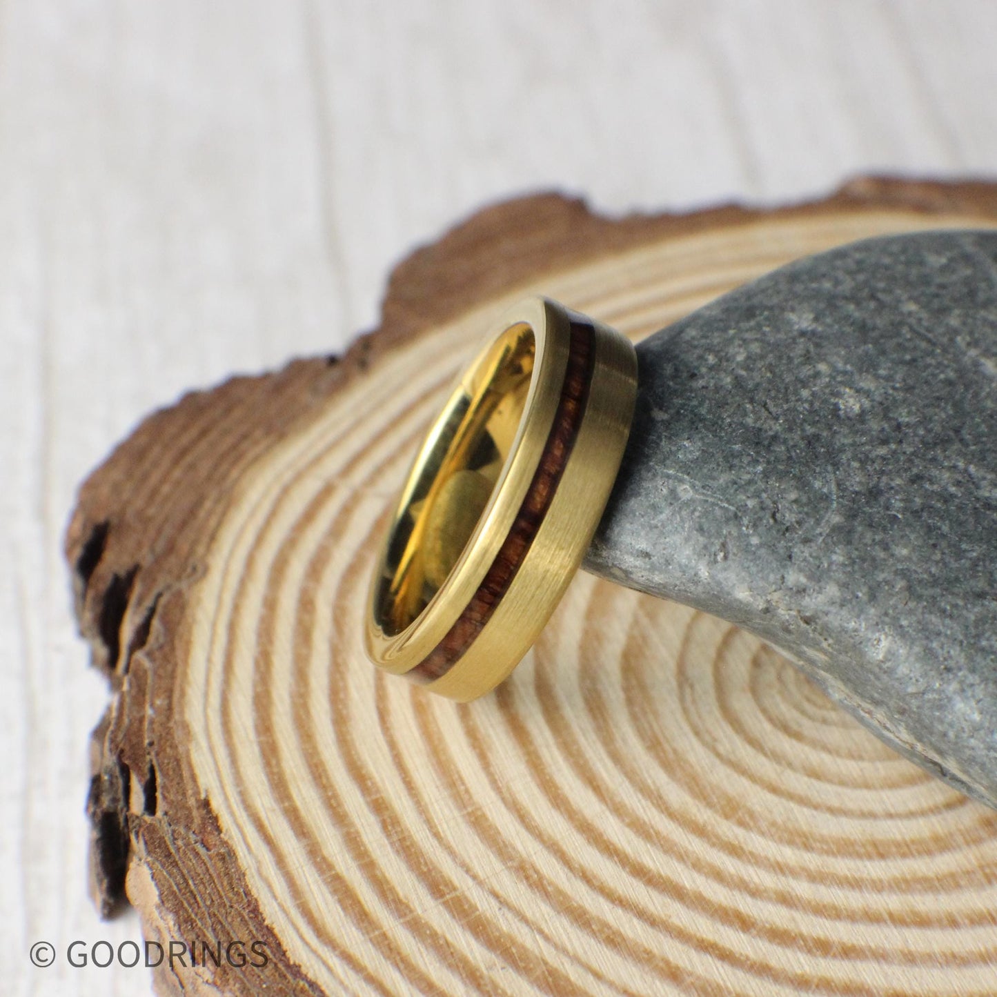 Displayed on smooth stone, the gold tungsten ring features an offset strip of genuine Hawaiian Koa wood. This detailed view emphasizes the ring’s craftsmanship and elegant balance of ruggedness and sophistication. Perfect for grooms or nature lovers.