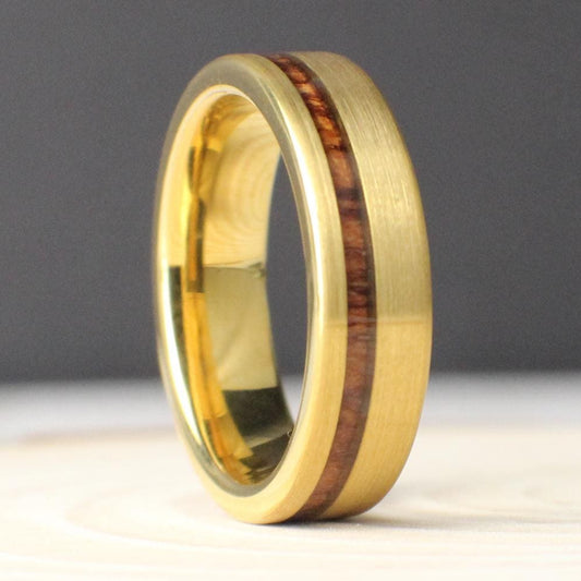 A gold-plated tungsten men’s ring with an offset Hawaiian Koa wood inlay. The rich reddish wood contrasts beautifully with the brushed gold finish. The 6mm wide band is designed for comfort and strength, perfect for weddings or everyday wear. Durable, stylish, and meaningful.